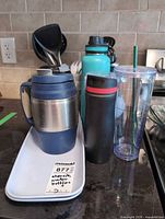 Front view of assorted drinkware pieces on tray including travel mugs, water bottle and tumbler