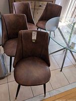 Four brown faux leather dining chairs around a glass table