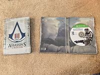 Front of AC III steelbook and open Battlefront steelbook showing disc