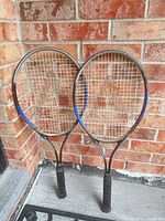 Front view of two tennis racquets leaning against brick wall
