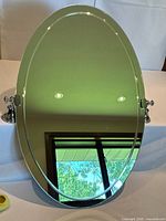 Full view of oval mirror standing vertically showing mounts and glass surface