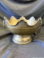 Front view of brass bowl showing scalloped rim, lion head handle, pedestal base