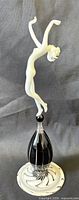 Full view of sculpture showing white nude figure atop black pedestal and spiral base