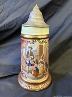 Front view of stein showing painted scene, pewter lid and decorative borders