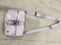 Full view of crossbody bag front showing strap, buckle, pockets, logo