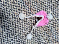 Pink knit dog hat with pom-poms on woven rug