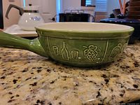 Green handled sauté pan with embossed grape and bottle design
