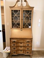 Front view closed showing glass doors, drop front, drawers and feet