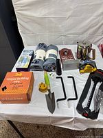 All items laid out on table: sprinkler, trowel, towels, bottle opener sign, coffee pot, coupler lock, wire box, RV filter, screw hooks