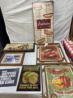 All seven wall hangings displayed on table including metal signs, hot dog sign, framed prints