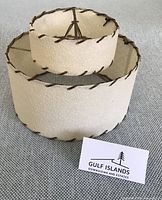 Two-tier cream fabric clip-on lampshade with brown whipstitch trim, business card for scale