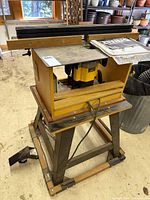 Overall view of router table on stand with router mounted underneath and manual on top