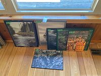 Five framed posters/prints leaning against window including four Algonquin Park scenes and one Orient Express