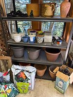 Full shelving unit with various planters, soil bags, watering device, hose and tools