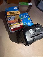 Fellowes shredder and open box containing paper reams, sheet protectors, folders