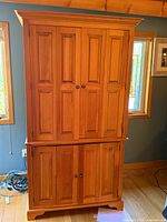 Front view of closed armoire showing paneled doors, crown and base