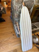 Full view of ironing board standing upright with striped cover visible