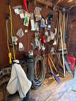 Wide view of pegboard wall with long-handled tools, blower tubes, hose, gas can