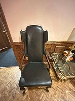 Front view of black faux leather wingback armchair with wood claw legs