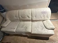 Top view of full sofa showing cream faux leather upholstery and overall wear