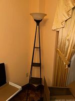 Full view of black metal floor lamp with shelves and white glass shade
