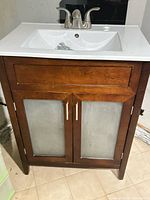 Front view of vanity showing wood finish, frosted glass doors, metal pulls, integrated sink and faucet