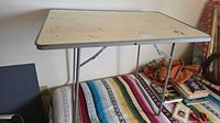 Full view of folding table on bed showing laminate top and legs