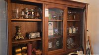 Cabinet view showing assorted branded glassware, liquor bottles, metal box, candlestick, wicker basket, candles