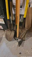 Group of shovels with yellow fiberglass and wood handles showing metal heads