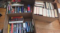 Two cardboard boxes filled with assorted hardcover and paperback books, spines visible