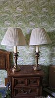 Pair of matching brass table lamps with pleated white-cream shades on wooden nightstand