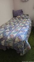 Twin bed fully made with patchwork comforter and pillow