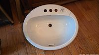 Top view of oval white sink showing three faucet holes, drain, overflow