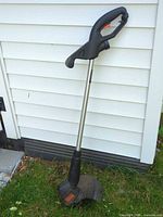 Full view of Black+Decker string trimmer leaning against siding