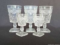 Front view of all five clear pressed glass goblets displaying size variation and pattern