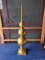 Full view of gold metal finial on blue surface against screen backdrop