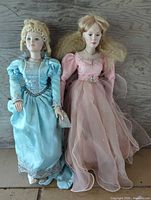 Two porcelain dolls standing side by side showing full outfits