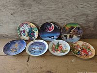 Group view of seven decorative porcelain plates with Christmas scenes, gold rims