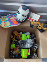 Box containing Mec shooter on top of assorted toy vehicles