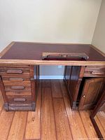 Full view of oak pedestal desk showing drawers, leather top, accessory rail resting on surface