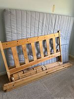Disassembled pine bed frame leaning against wall with mattress