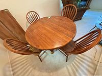 Overhead view of round solid wood table with four chairs and one leaf inserted
