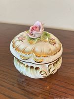 Full view of closed porcelain trinket box showing rose finial and gilt accents