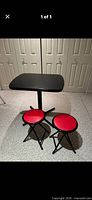 Full view of black pedestal table with two red round-seat folding stools