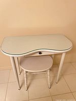 Front view of kidney-shaped white painted vanity table with matching stool underneath