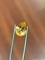 Front view of pear-cut golden citrine held by tweezers