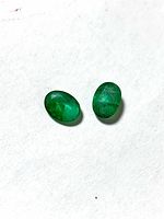 Two oval green emeralds on white background