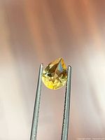 Front view of golden yellow pear-cut citrine held in tweezers