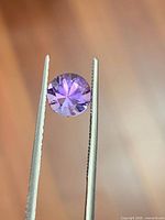 Front view of faceted amethyst held by tweezers