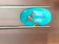 Side view of turquoise cabochon held in tweezers shows blue color and brown matrix